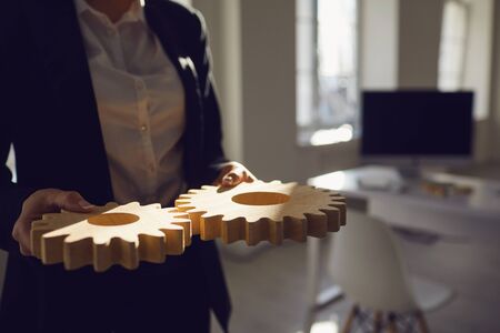 Faceless Businesswoman holding wooden gears in his hands in the office with windows. Planning team...