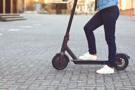 Young man in a helmet rides an electric scooter on a city street in summer.の写真素材