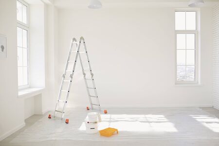 Painting in a white room with windows with a stepladder and paints on the floor.の写真素材