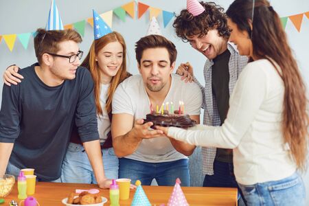 Happy Birthday party. A group of friends with a cake with candles wishes the man a happy birthday in...