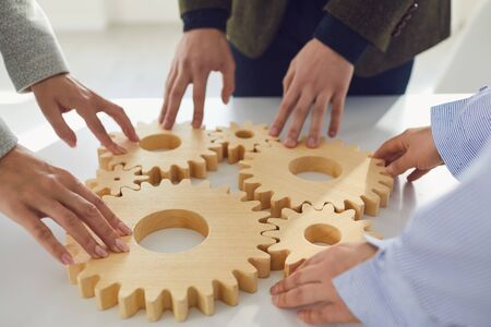 Faceless employees placing wooden cogwheels together on white table representing teamwork and coworkingの写真素材