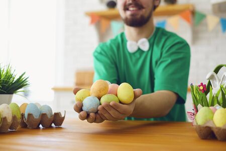 Happy Easter. A funny bearded man in a green T-shirt holds eggs in his hands and sits in the decorated room with the ears of a rabbit.の写真素材