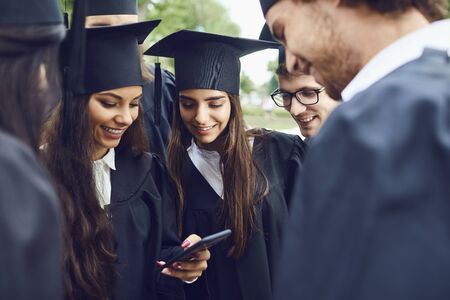 A group of graduates looking in mobile photo smiling against the background of the green trees....
