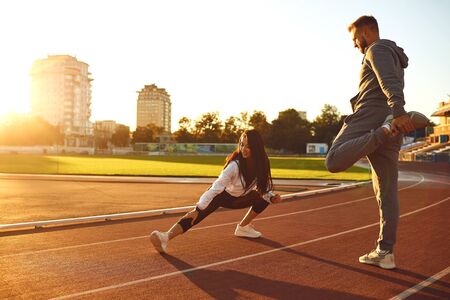 Couple in sportswear doing warm-up at the stadium in the morning in the summer and autumn.