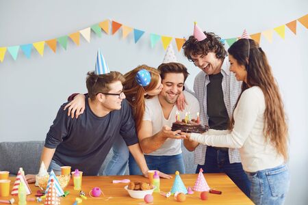 Happy Birthday party. A group of friends with a cake with candles wishes the man a happy birthday in...