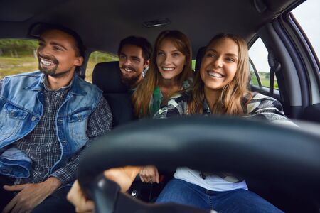 A group of happy friends travelers are driving in a car on road.の写真素材