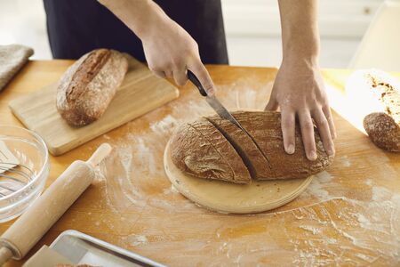 Hands cutting fresh homemade bread on a table in a bakery kitchen. Baker cuts bread.