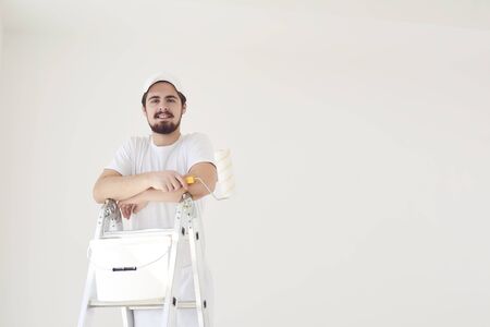 A male painter in a white uniform with a roller works in his hand in a white room.の写真素材