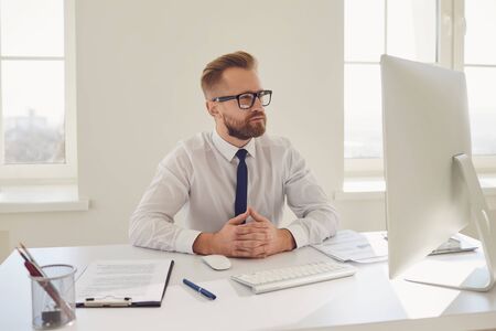 Serious busy businessman in glasses in a white shirt working sitting at a table with a computer in the office.の写真素材
