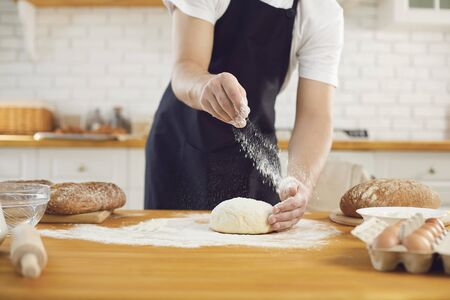 Baker male bearded man makes fresh bread dough while standing at a table in the kitchen bakery.