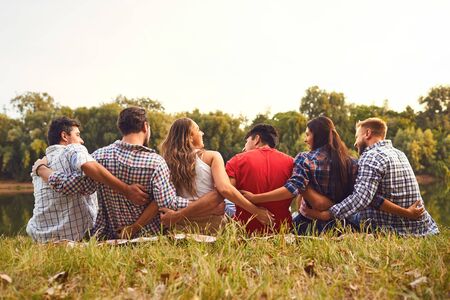 Rear view Young people sit on the grass hugging in nature in the park in autumn summer.の写真素材