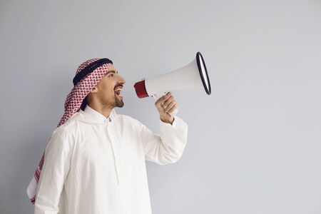 Arab man with a megaphone in hand shouting calls advertises offers on a gray background for text.の写真素材