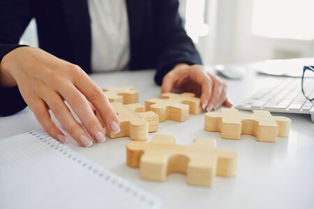 Faceless hands of a businesswoman with wooden puzzles on a white table in the office.with windows. Planning team strategy analysis idea solution concept.の写真素材