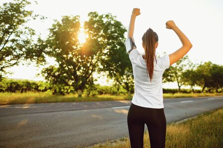 Young athletic smiling girl raised her hands up at a training on the nature. Active lifestyle.の写真素材