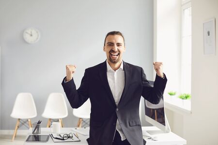 Joyful young Arabian male entrepreneur in formal wear celebrating achievement and looking at camera...