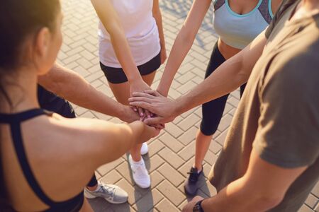 Group of sporting people join hands in the park at training. Union sports team of people. Sport club of young people. A team of athletes training together.の写真素材