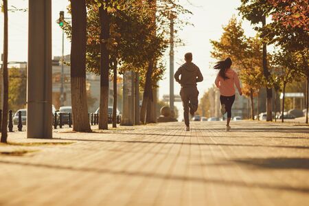 A man and a woman in sportswear are running along the city street in the morning. Runners are running in the city..Jogging. Health. Healthy lifestyle.の写真素材