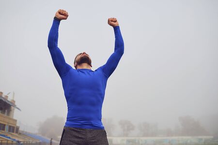 The guy the athlete raised his hands up at the stadium in the fog. The concept of victory of success motivation good luck in sports.の写真素材