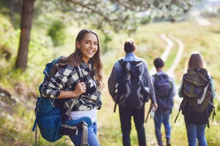 Young girl with a backpack with friends, tourists walking in nature.