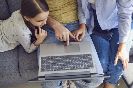 Close-up top view of a happy family using laptop while sitting at home. Parents and daughter watch...