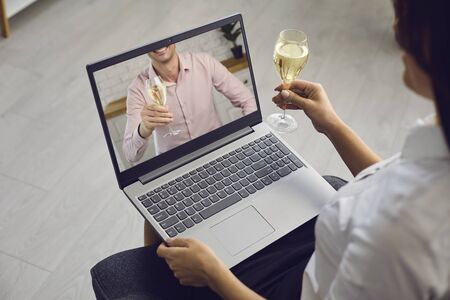 Date online. Loving couple with glasses of wine on a date distance using a video call laptop in a romantic setting at home. St. Valentines Day.の写真素材