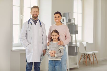 Happy family on a visit to the doctor in the office of a doctor. Male family doctor sitting at the table with smiling family at the clinic.の写真素材