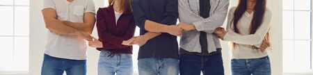 A group of people hold each others hands while standing against the background of a gray wall....