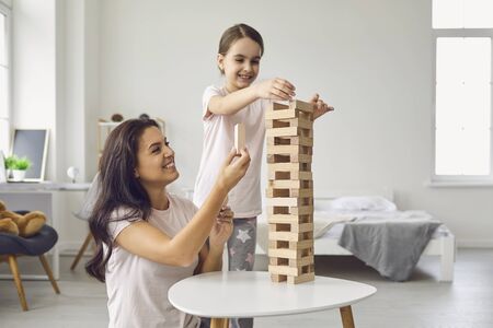 Mother and daughter in pajamas play board games while sitting at a table in the living room. Happy mothers day. Mom and quarantined daughter in the apartment.の写真素材