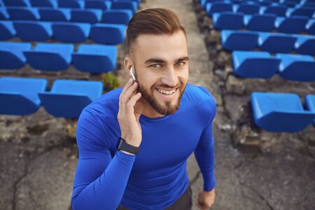 Portrait of a young happy male athlete in headphones and a clock at a stadium in the fog. The...