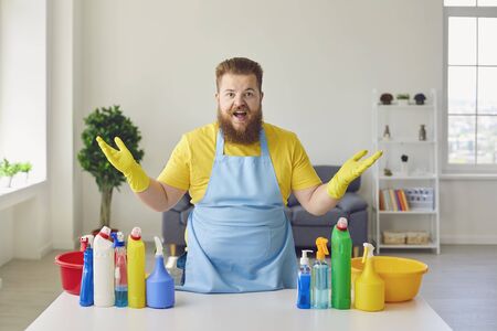 Funny fat man in an apron and yellow cleaning gloves is cleaning the house in the room home office.の写真素材