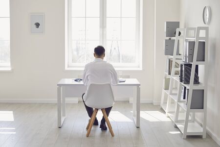 Doctor works in a white office clinic back view. Confident serious doctor works at the workplace in the hospital. Profession medical worker therapist pediatrician cardiologist.の写真素材