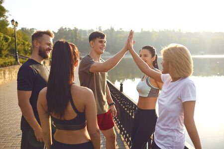 A group of young people in sportswear put their hands together while standing in a park in the...