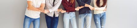 A group of people hold each others hands while standing against the background of a gray wall. Concept community support team help bonding friendship teamwork.の写真素材