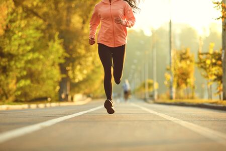 A girl in sportswear runs on the road in the autumn park. Running in the morning. Jogging during training.の写真素材