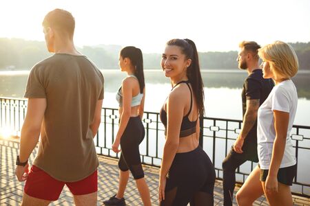 A group of young athletes are smiling standing on the background of a lake in a city park in autumn summer. Healthy lifestyle.の写真素材