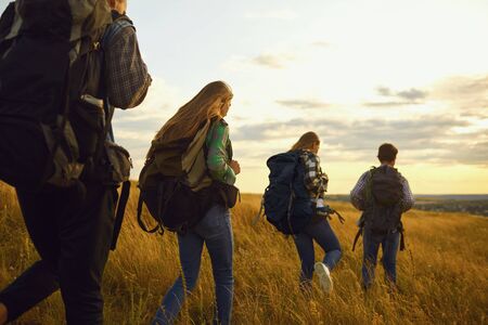 Young people with backpacks stand in the forest from behind. Tourists on the tourist route.