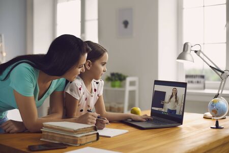 Online school. Family mother and girl watching lesson conference teacher remotely sitting at table at home. Education for schoolchildren children online video call with laptop. School remotely online internet educational video lecture.の写真素材