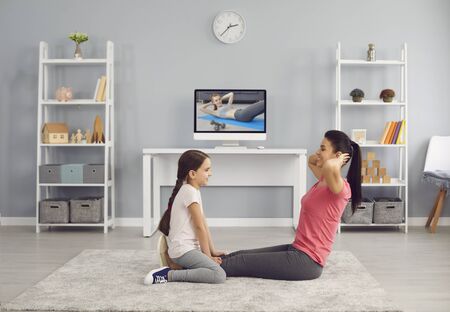 Happy mother and daughter working out together to video tutorial on TV at home. Cheerful family fitness exercising in light room. Happy family at training sport video course chat call online in living room. Healthy lifestyle conceptの写真素材