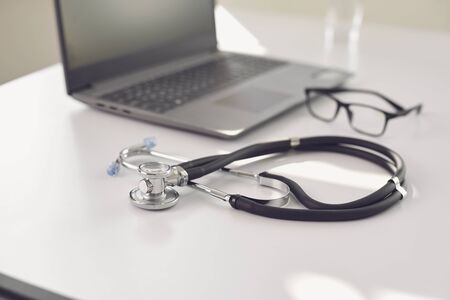 Doctor online. A stethoscope is on a white table with a laptop in blur at the hospital office. The concept of medical consultation for patients call to medical services. Consultation diagnosis remote sensing survey analysis of prescription medical insurance for sick people patients.の写真素材