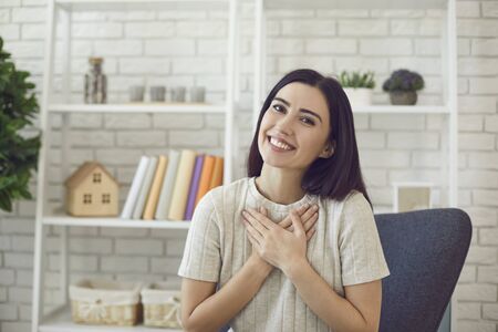 Online communication. Sincere young girl talking to her family or friends through webcam, putting hands on her heart, feeling happy at homeの写真素材