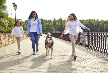 Happy mother with two daughters walking their dog on riverside. Cheerful parent with kids and pet in city park. Family bonding conceptの写真素材