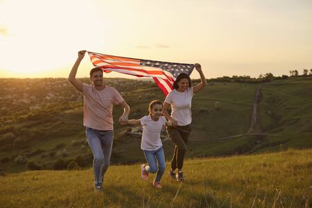 Patriotic holiday Independence Day of America. A cheerful family is having fun running along the grass in a summer park. USA July 4th Celebration.の写真素材