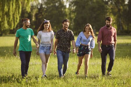 Full length portrait of happy young friends walking in countryside on warm summer day. Group of...