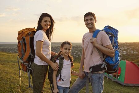 Young family of three with backpacks at campsite in mountains. Portrait of happy parents and their daughter enjoying summer hiking tripの写真素材
