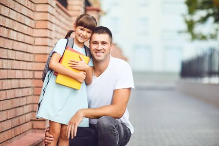 Schoolgirl with father smiling outdoors at school. First day back to school.の写真素材