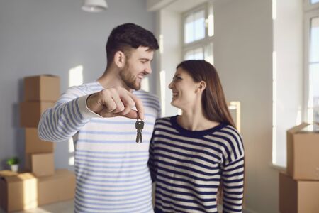 Happy couple with keys to new home in hands smiling while standing in room. Concept of buying sale...