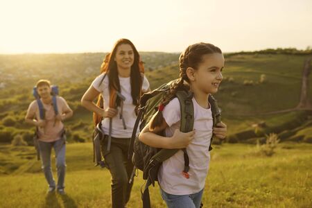 Family with a child with backpacks on a walk in nature at sunset. Mother father and daughter travel camping in the mountains.の写真素材