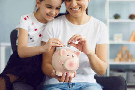 Family finance money saving concept. Mate and child lay money in a piggy bank pig sitting in a chair at home.の写真素材