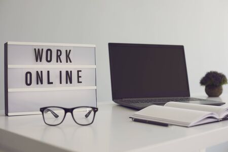 WORK ONLINE sign and laptop computer with blank screen on desk at home office, mockup for your design. Freelancer or blogger workplaceの写真素材