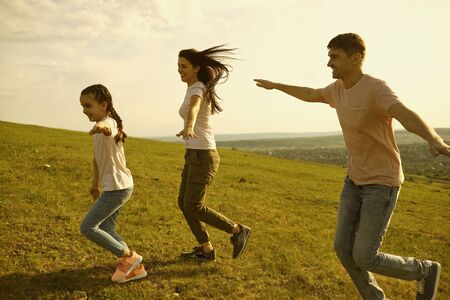 Joyful family with mom, dad and little kid running in mountains. Parents with their child having fun playing airplane game outdoorsの写真素材